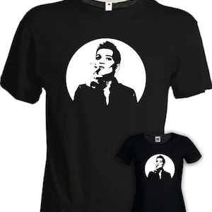 Può includere: T-shirt neri con grafica bianca di una persona che fuma, posta all'interno di un cerchio bianco. Il disegno è ripetuto su una t-shirt nera più piccola e aderente. Entrambe le magliette hanno maniche corte e girocollo.