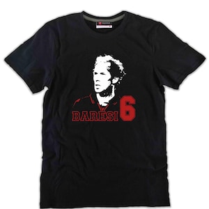 Peut inclure: Un t-shirt noir à manches courtes et col rond arborant un portrait graphique blanc d'un homme. Sous le portrait, le texte BARESI est imprimé en rouge, accompagné du chiffre rouge 6. Le t-shirt présente une coupe standard avec un col côtelé.