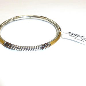 Puede incluir: Pulsera de brazalete plateada con una banda dorada y detalles en espiral. La pulsera presenta secciones adornadas con peque&ntilde;os cristales marrones y transparentes brillantes. Una etiqueta blanca con un c&oacute;digo de barras est&aacute; adjunta.