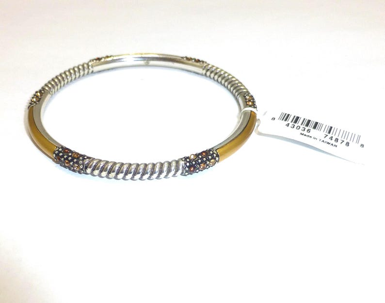 Puede incluir: Pulsera de brazalete plateada con una banda dorada y detalles en espiral. La pulsera presenta secciones adornadas con peque&ntilde;os cristales marrones y transparentes brillantes. Una etiqueta blanca con un c&oacute;digo de barras est&aacute; adjunta.