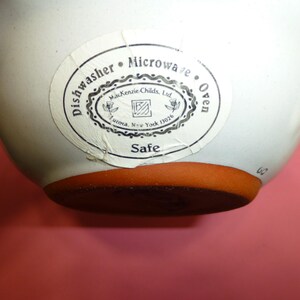 K&ouml;nnte beinhalten: Eine wei&szlig;e Keramiksch&uuml;ssel mit braunem Boden. Ein Aufkleber auf der Sch&uuml;ssel lautet "Dishwasher Microwave Oven Safe" und "MacKenzie-Childs, Ltd. Aurora, New York 13026."