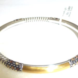 Puede incluir: Pulsera de brazalete plateada con una secci&oacute;n central dorada. La pulsera presenta un dise&ntilde;o de cuerda trenzada en los laterales y est&aacute; adornada con peque&ntilde;as piedras brillantes de color marr&oacute;n y dorado. Una etiqueta est&aacute; adjunta.