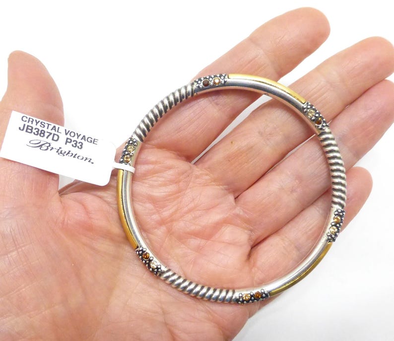 Puede incluir: Una pulsera de brazalete plateada con un dise&ntilde;o de cuerda trenzada y detalles dorados. La pulsera presenta peque&ntilde;os adornos redondos de color &aacute;mbar. La etiqueta dice "Crystal Voyage JB387D P33 Brighton."