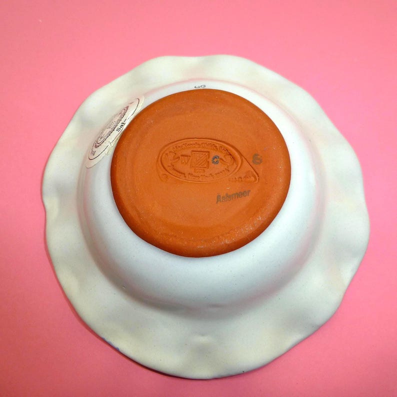 K&ouml;nnte beinhalten: Eine wei&szlig;e Keramikschale mit gewelltem Rand, von unten betrachtet. Das Innere ist in einem warmen Terrakottafarbton gehalten, mit einem gestempelten Design und dem Wort "Anismeer". Die Schale hat eine leicht unregelm&auml;&szlig;ige Form.