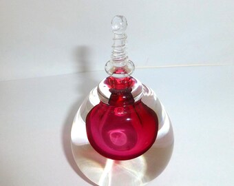 May include: A clear glass perfume bottle with a rounded base and a deep red spherical centre. The bottle features a clear glass stopper with a spiraled, tapered top that extends upwards from the centre of the red glass sphere.