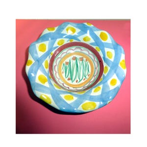 K&ouml;nnte beinhalten: Eine dekorative Keramikschale mit gewelltem Rand. Die Schale hat ein blau-wei&szlig;es Webmuster mit gelben Akzenten. Die Mitte der Schale hat ein Blumendesign mit roten, gr&uuml;nen und orangen Farben.