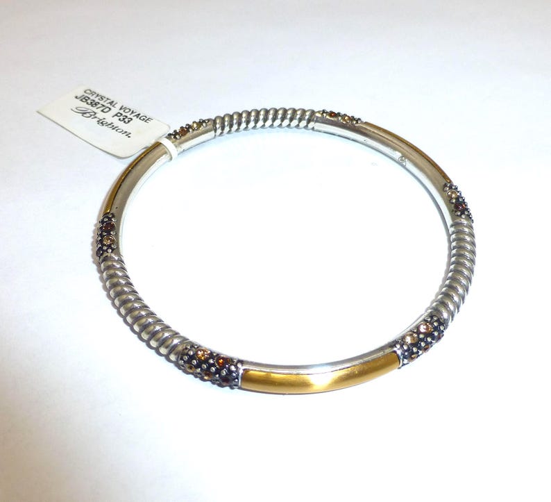 Puede incluir: Pulsera plateada con dise&ntilde;o de cuerda trenzada y detalles dorados. La pulsera presenta peque&ntilde;os cristales de color marr&oacute;n y una etiqueta que dice "Crystal Voyage JB387D P33 Brighton."