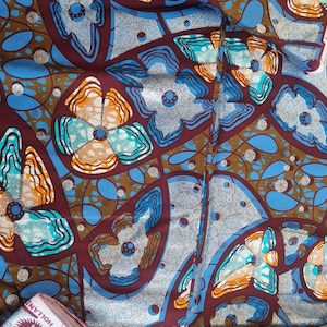 May include: A fabric featuring a repeating pattern of stylised flowers in shades of orange, turquoise, and light blue, set against a deep maroon background with interconnected brown lines and silver-toned circular accents throughout the design.