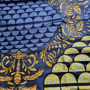 May include: A close-up of fabric featuring a repeating pattern of blue semi-circles and yellow floral designs on a dark blue background. The fabric has a textured appearance and a mix of geometric and organic shapes.