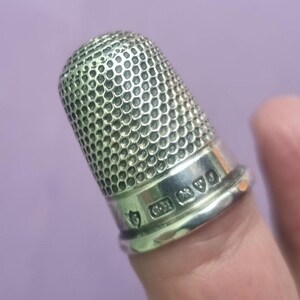 May include: A silver thimble with a textured surface and hallmarks on the base. The hallmarks include a crown, a lion, and a letter.