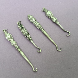 Puede incluir: Cuatro herramientas de cuerno de zapato de plata con mangos ornamentados. Los mangos están decorados con diseños florales. Las herramientas tienen aproximadamente 10 cm de largo.