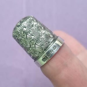 May include: A silver thimble with a floral design. The thimble is engraved with the letters "E.S."