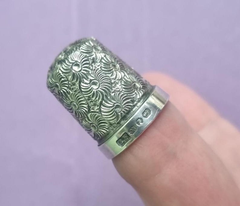 May include: A silver thimble with a floral design. The thimble is engraved with the letters "E.S."