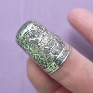 May include: A silver thimble with a decorative floral pattern and the inscription "925" on the side.