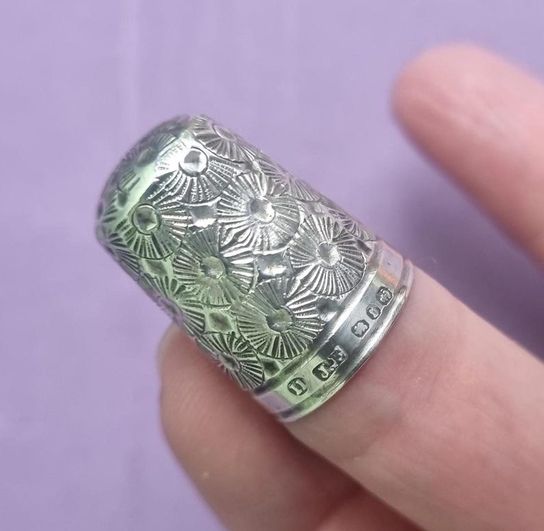 May include: A silver thimble with a decorative floral pattern and the inscription "925" on the side.
