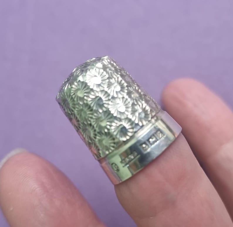 May include: Silver thimble with a floral design and the inscription "925" on the side.
