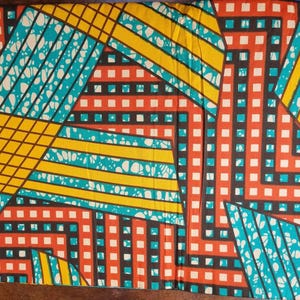 May include: A colourful fabric with a geometric design. The pattern incorporates intersecting lines and shapes in yellow, teal, black, and red. The fabric's design includes squares and diagonal stripes, creating a striking visual.