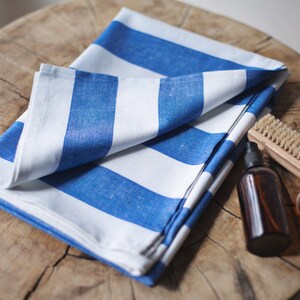 May include: A white and blue striped fabric towel folded on a wooden surface. A small brown bottle and a wooden brush with natural bristles are also on the surface.