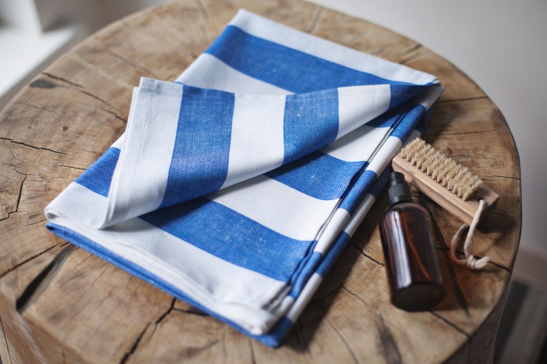 May include: A white and blue striped fabric towel folded on a wooden surface. A small brown bottle and a wooden brush with natural bristles are also on the surface.