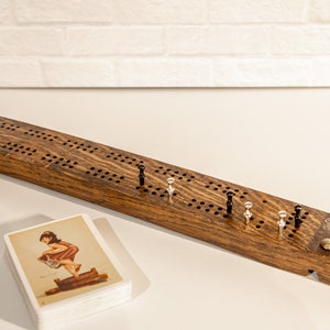 May include: A wooden cribbage board with black and silver pegs. The board has a dark wood finish and is made of solid wood. The board is on a white surface.