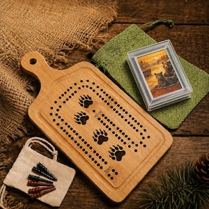 Può includere: Una tavola da cribbage in legno a forma di tagliere con quattro intagli a forma di zampa d'orso, fori per il punteggio e le parole Start e Winner. Include un mazzo di carte in una custodia di plastica, un sacchetto e quattro pioli.