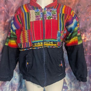 May include: A colorful, multi-striped jacket with a zipper closure. The jacket is made of a patchwork of different fabrics and colors, including red, blue, green, yellow, and purple. The jacket has a black bottom with two pockets.