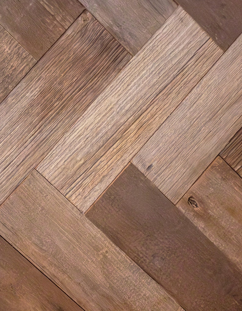 May include: Close-up of a herringbone pattern made of reclaimed wood planks. The planks vary in color from light tan to dark brown, with visible wood grain and knots. The pattern creates a textured, rustic appearance.