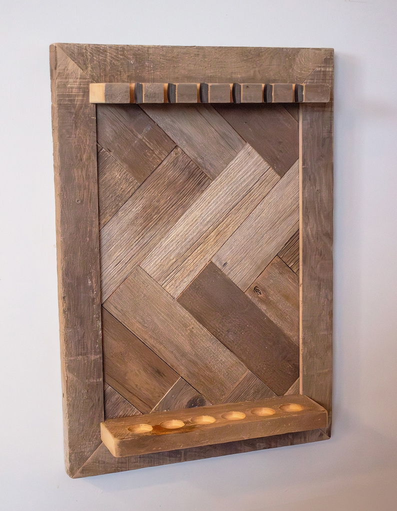 May include: A rustic wooden wall-mounted display rack. The rack features a herringbone pattern made of various shades of brown wood. It has a top shelf with six small square holes and a bottom shelf with six round holes.
