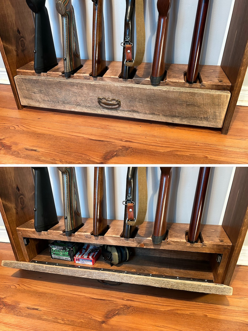 May include: A wooden gun rack with slots for several rifles. The rack features a drawer with a metal handle. The rifles are in various colours, including black, brown, and wood grain. The rack is made of stained wood.