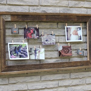 May include: A rustic wooden frame with a wire mesh insert holds a collection of photographs secured with clothes pegs. The photos feature a variety of subjects, including a wedding ring, a bouquet of flowers, and a couple.
