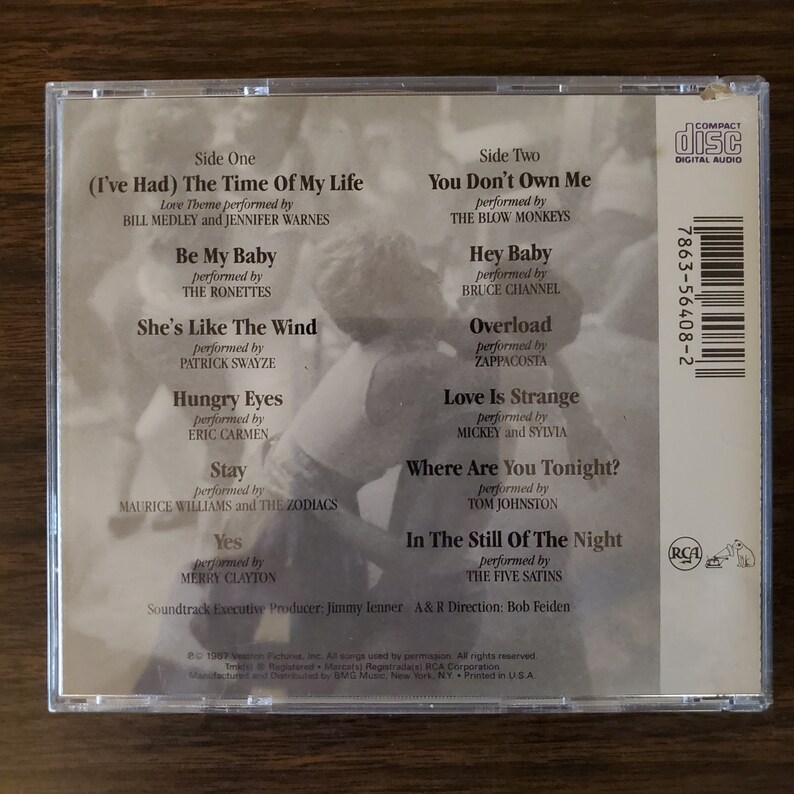 May include: The back of a compact disc case for the soundtrack to the movie "Dirty Dancing". The case is white with black text and features a photo of a couple dancing. The text includes the song titles and artists, as well as the album's executive producer and A&R director.
