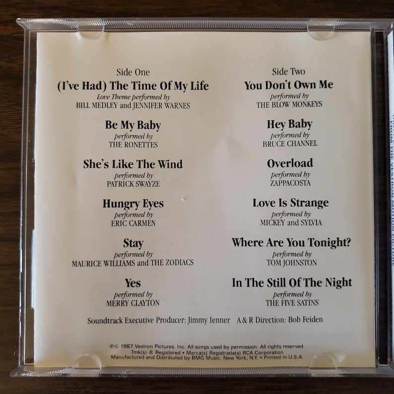 May include: A CD case with a white background and black text listing the songs and artists on the CD. The songs include "(I've Had) The Time Of My Life", "Be My Baby", "She's Like The Wind", "Hungry Eyes", "Stay", "Yes", "You Don't Own Me", "Hey Baby", "Overload", "Love Is Strange", "Where Are You Tonight?", and "In The Still Of The Night".