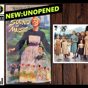 May include: A VHS tape of the Sound of Music movie, featuring Julie Andrews on the cover. The tape is new and unopened, with the title "The Rodgers & Hammerstein Sound of Music" and the words "NEW: UNOPENED" in yellow text. The image also includes a scene from the movie with Julie Andrews and the Von Trapp children.