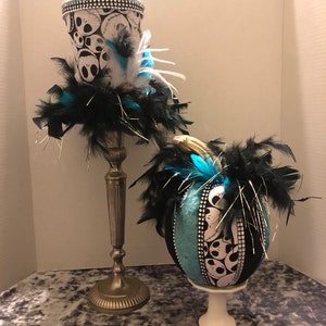 May include: Two Halloween-themed decorations, a black and white top hat with a blue and white skull pattern and a blue and white pumpkin with a skull pattern, both with black feathers.