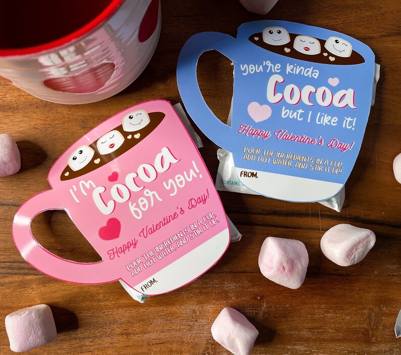 May include: Pink and blue cocoa-themed Valentine's Day cards shaped like mugs, with marshmallow faces in the cocoa. The pink card says "I'm Cocoa for you!" and the blue card says "You're kinda Cocoa but I like it!" with the text "Happy Valentine's Day!"