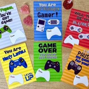 Peut inclure: Dix cartes de Saint-Valentin imprimables colorées sur le thème du jeu vidéo. Les cartes présentent des illustrations de manettes de jeu vidéo et le texte "Hey Friend, You've Got Game!", "You Are My Favorite Gamer!", "Will You Be My Player 2?", "You Are Next Level!", "Game Over You Are My Best Friend!", et "I'd Pause My Game For You!"