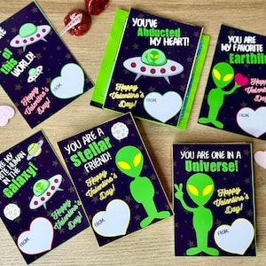 May include: Ten printable Valentine's Day cards featuring alien illustrations and space-themed messages. The cards have a black background with colorful stars and planets. The text on the cards includes phrases like "You are out of this world!" and "You are one in a universe!"