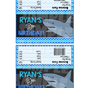 May include: A blue and white chevron patterned background with a black chalkboard. The chalkboard has the text "RYAN'S 9th BIRTHDAY!" and a cartoon shark. The nutrition facts label says "1 Shark Crew" and "Happy Birthday!"