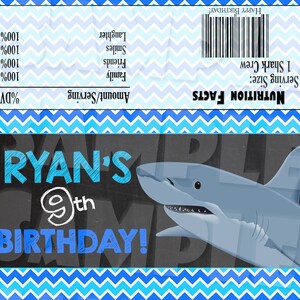 May include: A blue and white chevron patterned background with a chalkboard sign that says "Ryan's 9th Birthday!" with a cartoon shark illustration. The sign is on a blue and white chevron patterned background.