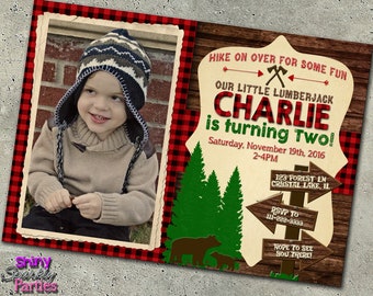 May include: A red and black plaid invitation with a photo of a young boy wearing a brown and blue knit hat. The invitation says "HIKE ON OVER FOR SOME FUN" and "OUR LITTLE LUMBERJACK CHARLIE is turning Two!" with the date and time of the party. The invitation also has a sign with the address and RSVP information.