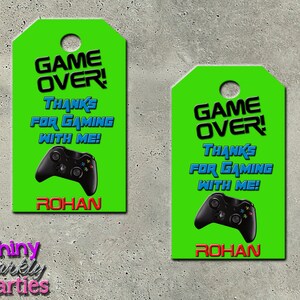 May include: Two green favor tags with the text "Game Over!" in black and blue. The tags also feature a black video game controller and the text "Thanks for gaming with me!" in blue. The name "Rohan" is printed in red at the bottom of each tag.