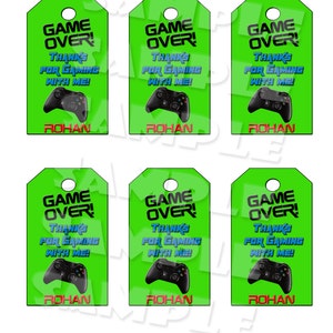 May include: Six green favor tags with the text "Game Over!" in black and white. The tags also feature a black and green video game controller and the text "Thanks for gaming with me!" in blue and white. The name "Rohan" is printed in red at the bottom of each tag.