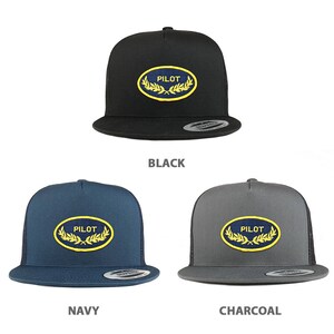 May include: Three trucker hats in black, navy blue, and charcoal gray. Each hat features a yellow embroidered laurel wreath with the word "PILOT" in the center.