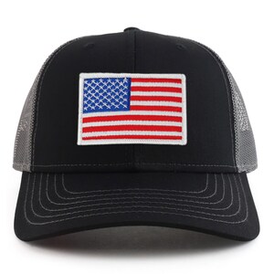 Op de afbeelding: Een zwarte en grijze truckercap met een rood, wit en blauw Amerikaans vlagpatch op de voorkant.