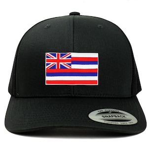 May include: Black trucker hat with a red, white, and blue Hawaiian flag patch. The hat has a black mesh back and a black snap closure. The hat also has a white sticker on the bottom that says "The Classics" and "Snapback" with the Yupoong logo.