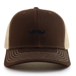 May include: A brown trucker cap with a black moustache embroidered on the front. The cap has a brown front panel and peak, with a beige mesh back and a curved peak with white stitching.