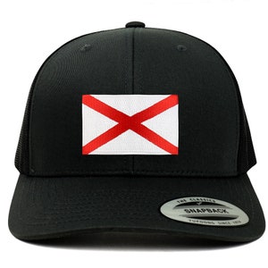 May include: Black trucker hat with a red cross on a white background. The hat has a black mesh back and a black snap closure. The hat is labeled "The Classics" and "Snapback" with the brand name "YUPOONG" and "Since 1974".
