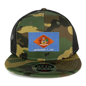 Pode incluir: Um boné de caminhoneiro de camuflagem preto e verde com um patch da bandeira do estado de Delaware azul e laranja. O patch tem o texto "DECEMBER 7, 1787" embaixo.