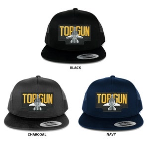 Puede incluir: Tres gorras de camionero con malla en la parte posterior. Las gorras son negras, carbón y azul marino. Cada gorra tiene un parche amarillo y blanco con el texto "TOP GUN" y una silueta blanca de un avión de combate.