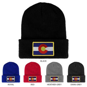 Pode incluir: Gorro de malha preto com um patch da bandeira do estado do Colorado. O patch apresenta uma borda dourada, um fundo listrado azul e branco e um emblema circular vermelho e amarelo. Gorros adicionais em azul royal, vermelho, cinza mesclado e cinza escuro também são mostrados.